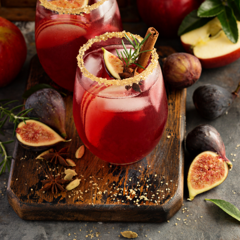 Red fall cocktails with sugared rims and cinnamon sticks, served with fresh figs and apples