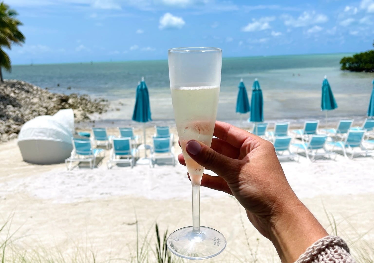 Hand holding a glass of prosecco overlooking the beach