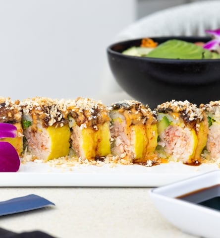 Sushi rolls topped with crunchy garnish and sauce, served with soy sauce